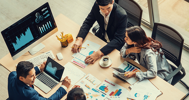 Group of employees seated around a cluttered table observing data