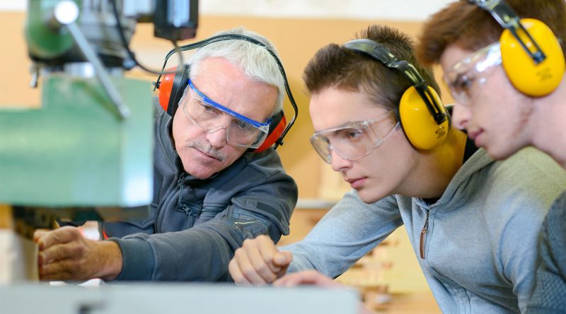 Image of an older man with construction ear protectors on showing two younger men in construction gear how to use a piece of machinery to support construction internships article