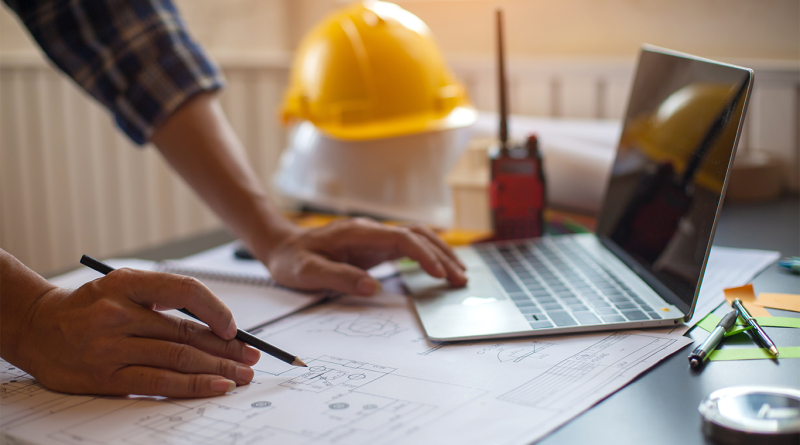 Image of a man leaning over a desk with laptop and hardhat to support Lendlease article