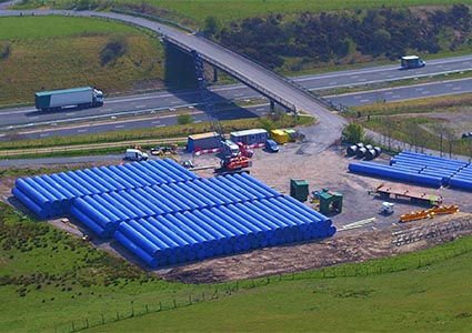 Many large blue pipes stacked next to dual carridgeway