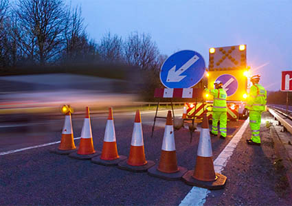 Road workers standing behind traffic cones & keep left sign