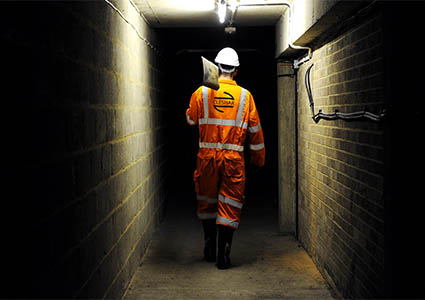 Cleshar worker walking in dark tunnel in orange overalls