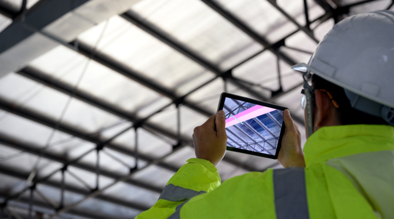 A construction professional using a tablet to view a Building Information Modelling (BIM) digital overlay on a structural ceiling.