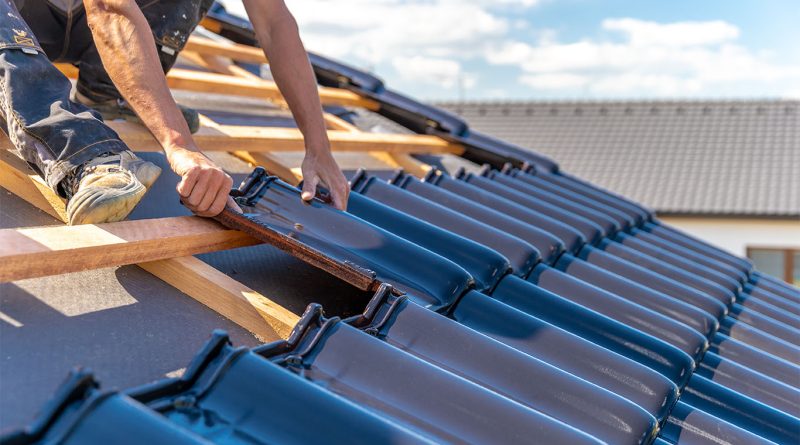 The top 10 roofing materials and their pros and cons Worker installing glossy clay roofing tiles on a wooden roof structure during a sunny day.