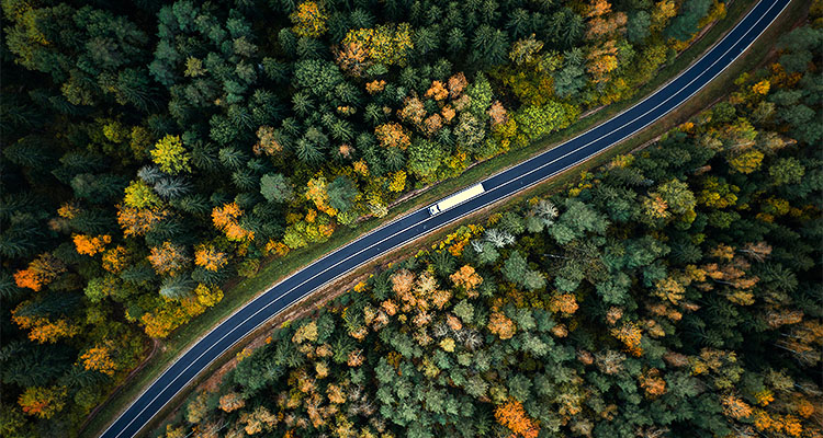 Arial view of heavy truck on a narrow twisting road. Autumn colorful trees by the sides of the road.