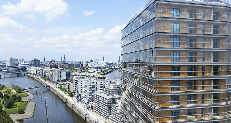 a modern, multi-story building with a facade of glass and timber, known as "Roots," located in Hamburg's HafenCity quarter