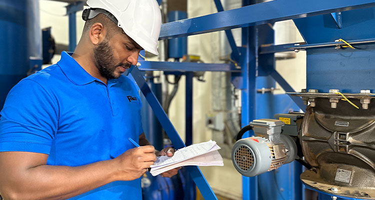 a person wearing a hard hat and a blue shirt while examining industrial machinery and taking notes