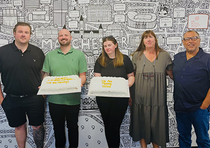 five people standing side-by-side in front of a large, illustrated wall mural
