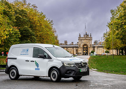  a white Renault Kangoo electric van parked on a paved path in front of a historic building
