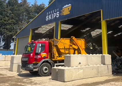 a yellow waste container truck parked at a Speedy Skips facility