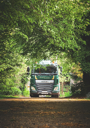  a BioMarsh Environmental green and white DAF commercial truck driving through a tree-lined road