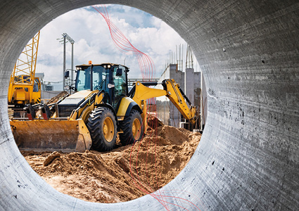  a yellow backhoe loader positioned at a busy construction site, viewed through a concrete pipe