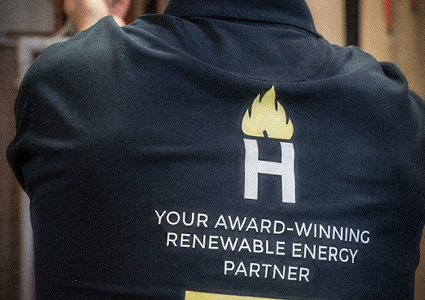 Heatforce branded black polo shirt features their "H" logo with a flame icon and the text "YOUR AWARD-WINNING RENEWABLE ENERGY PARTNER"