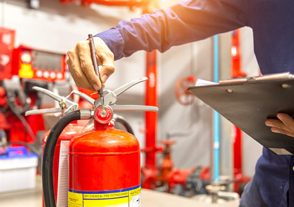 a technician inspecting a fire extinguisher's safety pin and pressure gauge