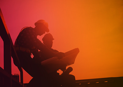 two individuals in silhouettes looking at a map against a warm-toned background