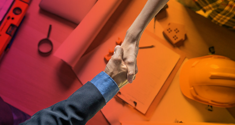 a handshake between two people over a desk filled with construction and architectural planning tools