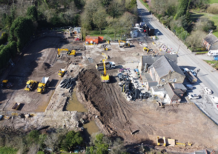 an aerial view of a construction site undergoing active groundwork and earthmoving phases next to an existing building