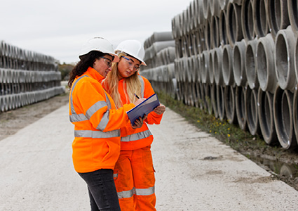 two civil engineering or construction professionals inspecting a site containing large stacks of precast concrete drainage pipes