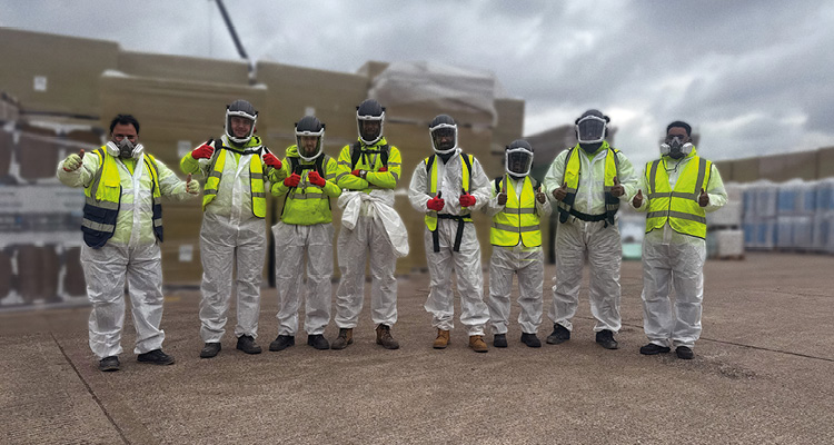 a team of workers in white disposable coveralls and yellow high-visibility vests posing for a photo on a concrete surface