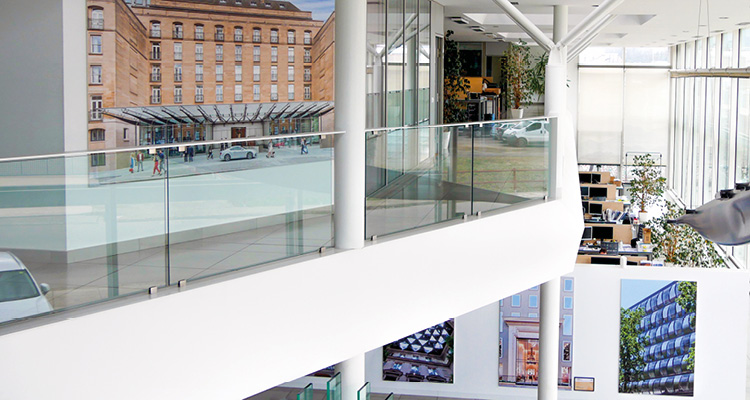 a modern structural glass balustrade system installed on an upper-level mezzanine walkway inside a contemporary atrium space