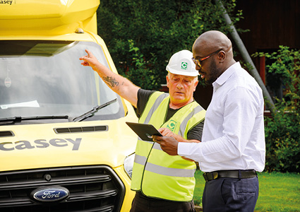 two men standing outdoors in daylight next to a bright yellow commercial vehicle, engaged in a professional discussion