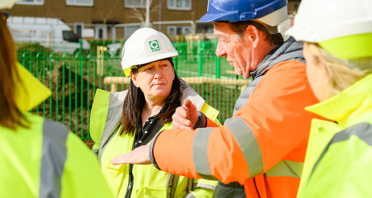 a group of construction and engineering professionals having an outdoor meeting on an active work site during a bright, sunny day