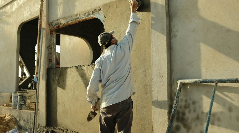 Construction worker applying material to an exterior wall during surface preparation work.