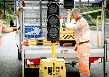 a road worker loading or unloading a portable battery-powered traffic light unit