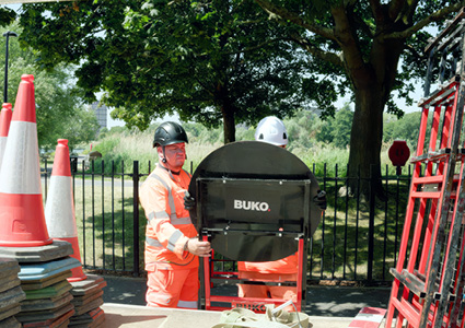 engineers setting up street safety barriers and a manhole cover or sign bearing the BUKO brand label