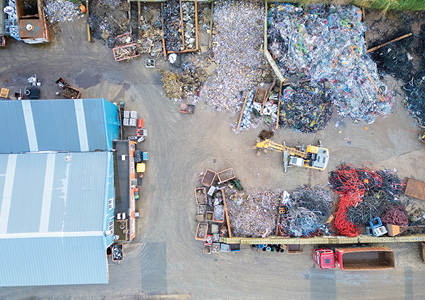  an aerial view of a waste management, scrap metal, or recycling facility featuring sorted material piles, skips, containers, and an excavator