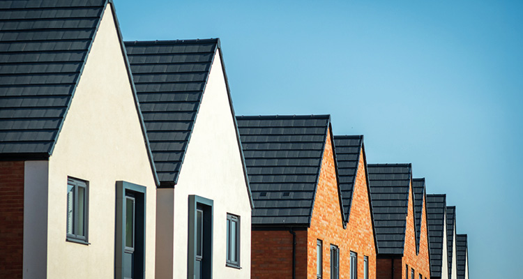 a row of newly built, terraced residential homes featuring alternating light-rendered and red-brick facades with steep gabled roofs and dark grey tiles