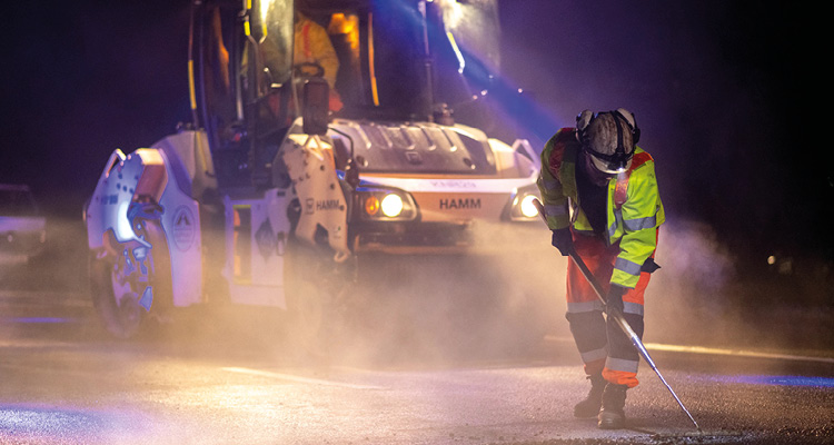 a night road resurfacing and maintenance operation featuring a Hamm tandem road roller and workers in high-visibility safety gear
