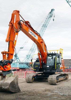a Hitachi ZX135US-7 tracked excavator featuring an orange boom, a black cab, and a heavy-duty bucket attachment on a job site