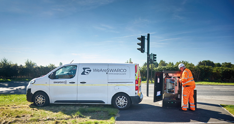 A SWARCO UK & Ireland engineer is maintaining a roadside traffic signal control cabinet and light system