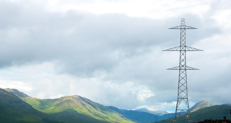 a high-voltage electricity transmission pylon standing in a green, mountainous landscape under a cloudy sky